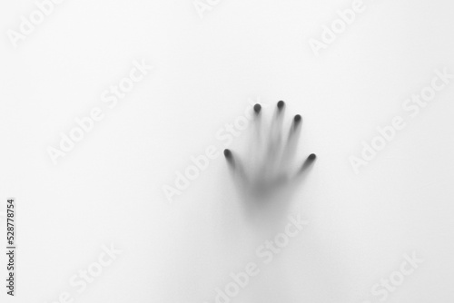Defocused hand silhouette behind frosted glass in black and white mode, halloween concept