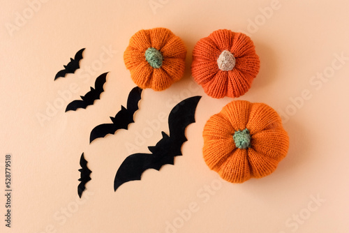 Leinwand Poster Knitted orange pumpkins with black bats on an orange background, autumn composition, flat lay
