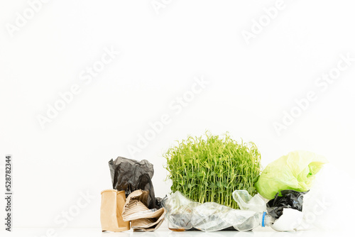 Fototapeta Naklejka Na Ścianę i Meble -  Small green plant grows through plastic trash on white background