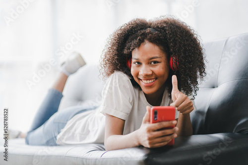 african american woman sitting on sofa at home video call chatting with friends using a laptop and a smartphone or phone