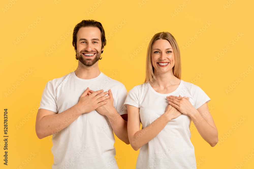 Smiling millennial caucasian family in white t-shirts press their hands to chest, isolated on yellow background Smiling millennial caucasian family in white t-shirts press their hands to chest, isolated on yellow background
