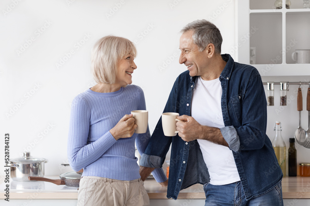 Obraz premium Loving senior couple in homewear drinking coffee at kitchen