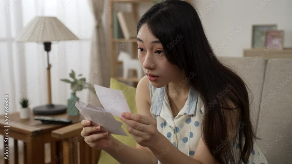lucky Asian woman watching televised draw and checking numbers is throwing lottery tickets in air while cheering for her win on living room sofa at home. lucky Asian woman watching televised draw and checking numbers is throwing lottery tickets in air while cheering for her win on living room sofa at home.