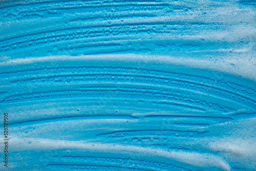 Foam swatch on a blue background. Soapy liquid texture with bubbles. Natural sunshine and shadows. Skin care cleansing cosmetic in top view.
