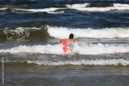 Dziecko z materacem dmuchanym wchodzi do morza na fale