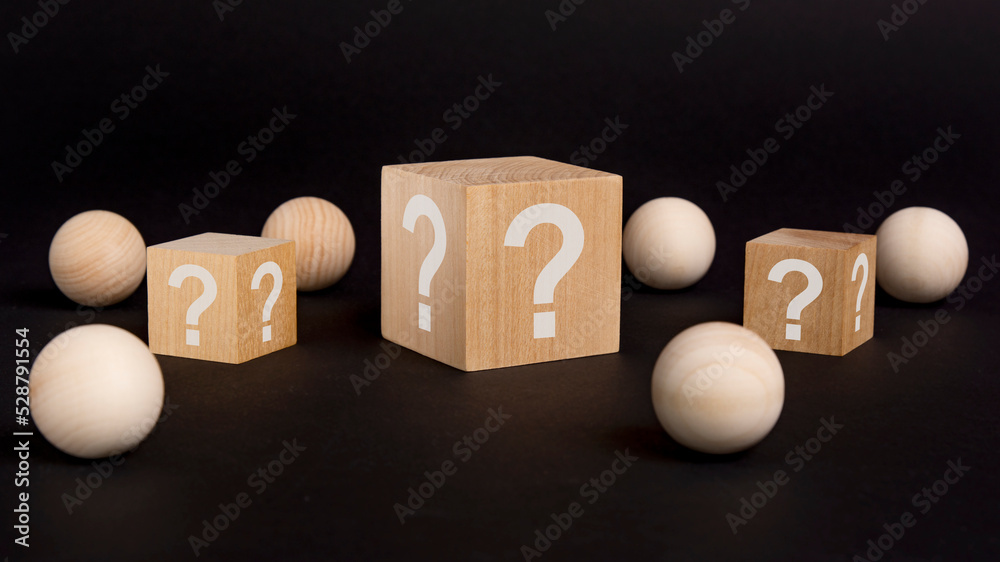 wooden cube with a question mark surrounded by wooden balls on a black table background wooden cube with a question mark surrounded by wooden balls on a black table background