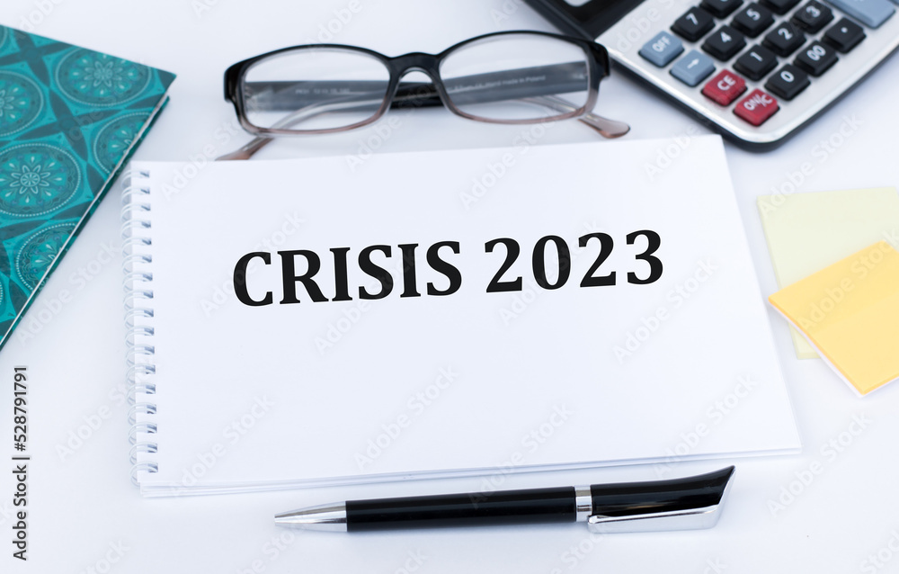 Crisis 2023 text on a notepad on a table next to a pen, glasses, calculator on a desk