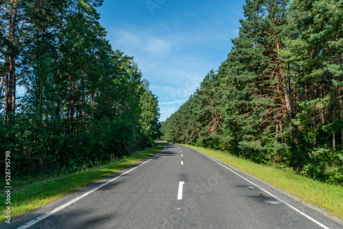 A new modern asphalt road passing through the forest. An empty country road in the woods. High-quality conditions for cargo and passenger transportation.