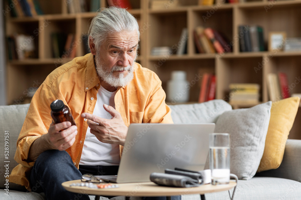 Fototapeta premium Elderly man seating on sofa, making distant video call