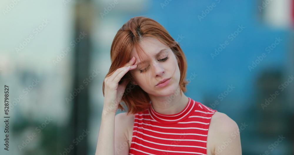 Tired young redhead woman feeling headache outside thinking deeply