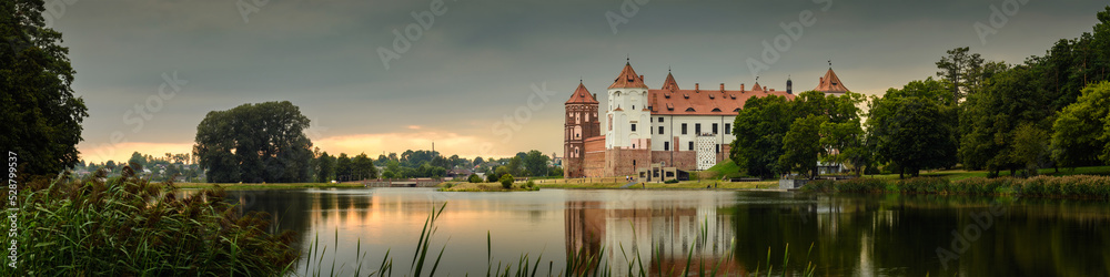 Mir Castle, Belarus. Scenic panoramic view of the complex across the lake with reflections on the water in the evening twilight. UNESCO world heritage