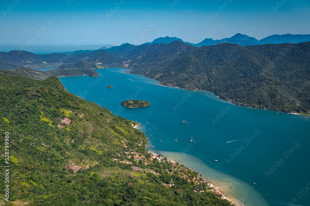 A lagoon with blue water and yachts, with a tropical forest, aerial view