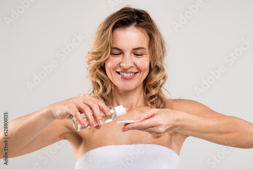 Skincare Routine. Smiling middle aged lady applying micellar water on cotton pad