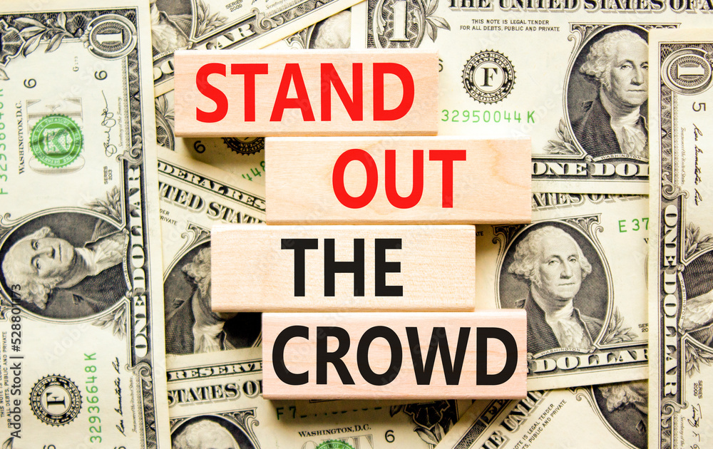 Stand out the crowd symbol. Concept words Stand out the crowd on wooden blocks on a beautiful background from dollar bills. Business, stand out the crowd concept