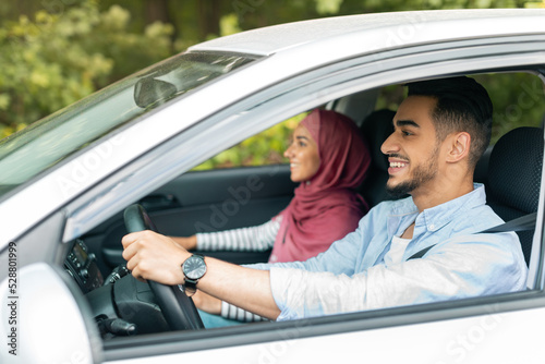 Happy millennial muslim wife in hijab and husband driving car at steering wheel, enjoy journey
