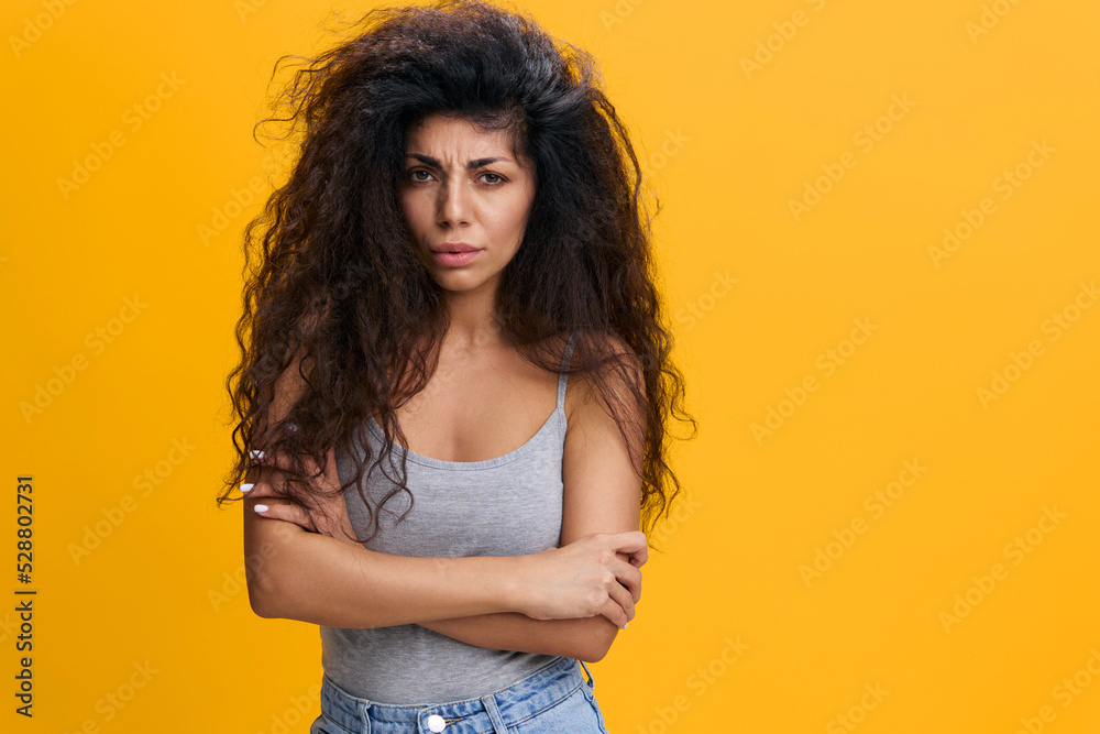 Grumpy Woman. Portrait of serious offended Latin lady standing with crossed arms, posing over yellow studio background, feeling angry and displeased, having bad mood, looking at camera, copy space Grumpy Woman. Portrait of serious offended Latin lady standing with crossed arms, posing over yellow studio background, feeling angry and displeased, having bad mood, looking at camera, copy space