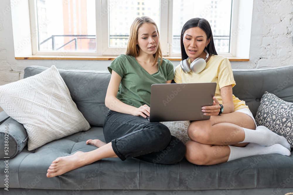 Two millennial diverse girl friends at home watching movies, browsing in the internet, shopping, spending fun time together, chat, talk. Females using technology. Asian and Caucasian model. Two millennial diverse girl friends at home watching movies, browsing in the internet, shopping, spending fun time together, chat, talk. Females using technology. Asian and Caucasian model.