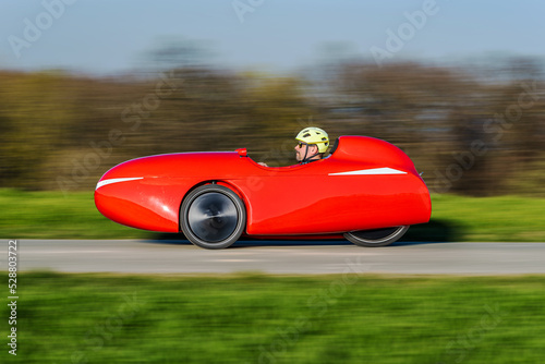 A red velomobile (recumbent tricycle) rushing by on a bikepath photo