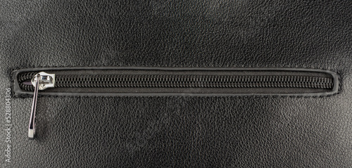 Closed zip fastening on black leather surface.