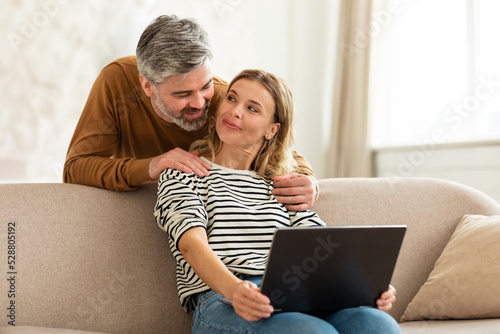 Happy Middle Aged Couple Using Laptop Computer At Home © Prostock-studio