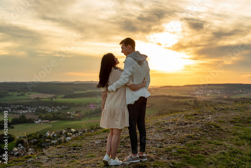 A couple in love stands on a mountain at sunset