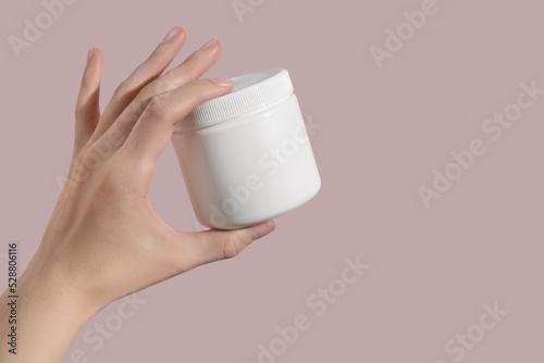 Hand holding blank white plastic supplement container on pink background. Package mockup blank for capsule.
