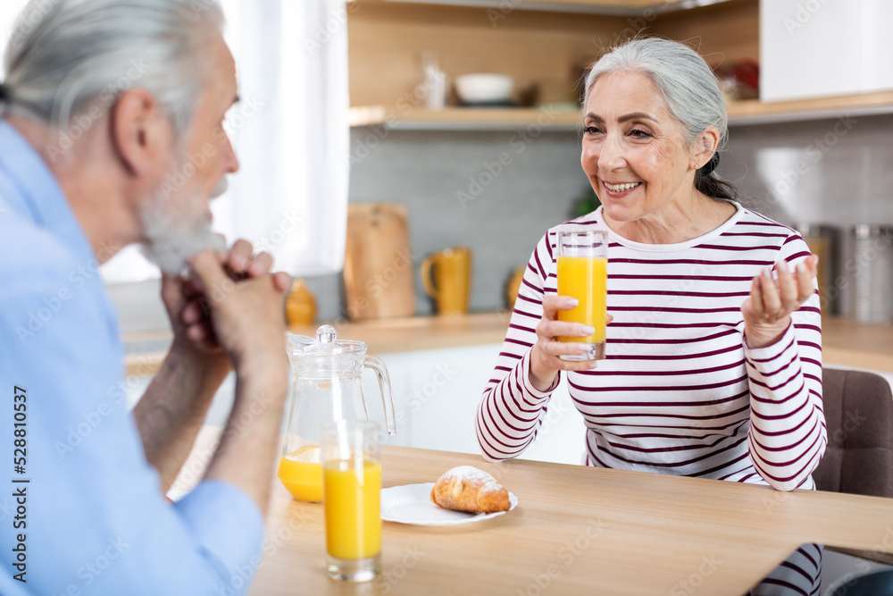 Happy Senior Spouses Chatting While Having Breakfast In Kitchen Together Happy Senior Spouses Chatting While Having Breakfast In Kitchen Together