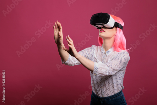 Cheerful woman using virtual reality glasses with 3d vision, interactive visual simulation on vr goggles. Electronic futuristic experience with augmented tech innovation over pink background. © DC Studio