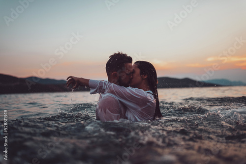 Obraz na plátně Romantic couple kissing in the sea at sunset. High quality photo
