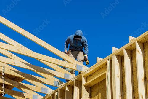 Fotografija A worker hammering wooden frame beams into rafters roof using an air hammer in h