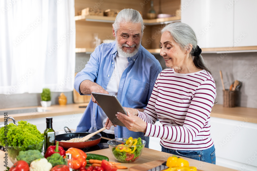Online Recipe. Happy Senior Couple Using Digital Tablet In Kitchen Together Online Recipe. Happy Senior Couple Using Digital Tablet In Kitchen Together