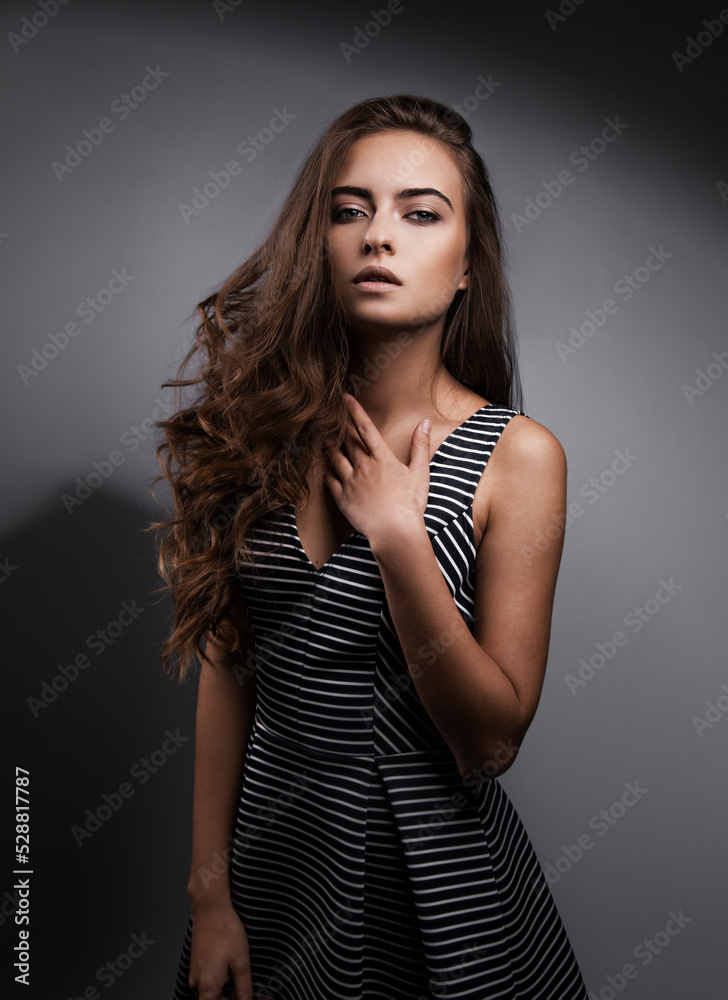 Beautiful romantic woman with nude natural makeup and long curly hair style posing in striped dress on grey background. Closeup portrait Beautiful romantic woman with nude natural makeup and long curly hair style posing in striped dress on grey background. Closeup portrait