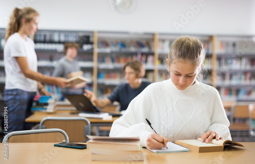 Portrait of teenager girl reading books and writing in notebooks in the library