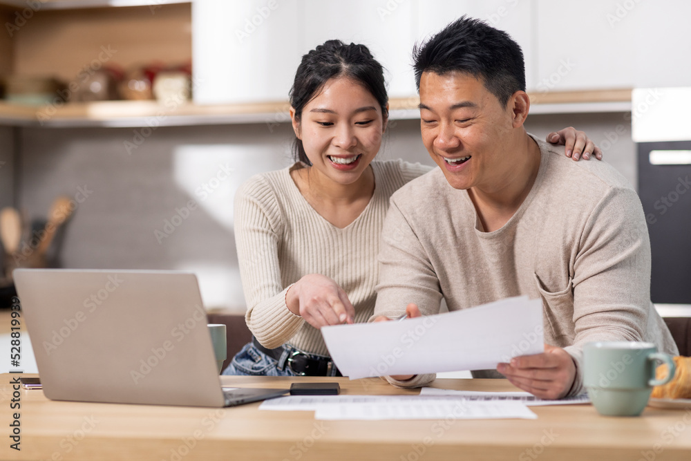 Cheerful asian spouses paying bills on Internet, using laptop Cheerful asian spouses paying bills on Internet, using laptop