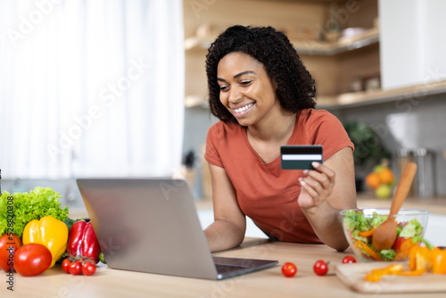 Satisfied young african american lady with laptop and credit card buy purchases remote  enjoy huge sale
