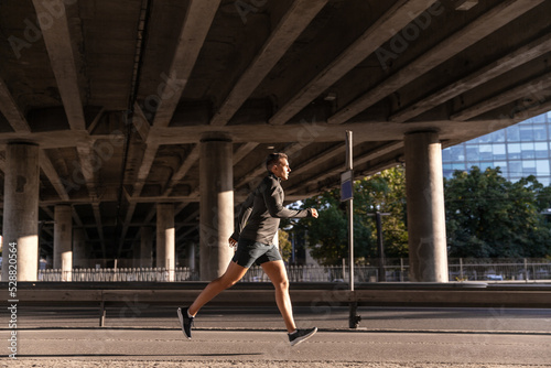 fitness, sport and healthy lifestyle concept - young man running outdoors under bridge