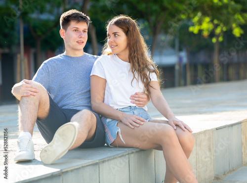 Young man is hugging his gerlfriend while they sitting on the step