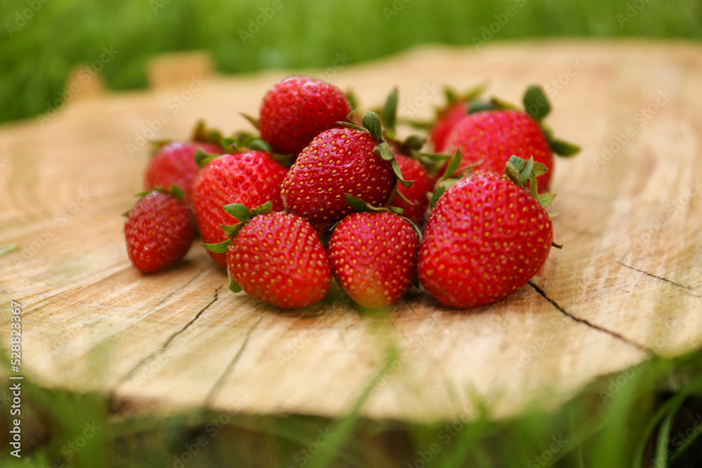 Pile of delicious ripe strawberries on tree stump outdoors, closeup