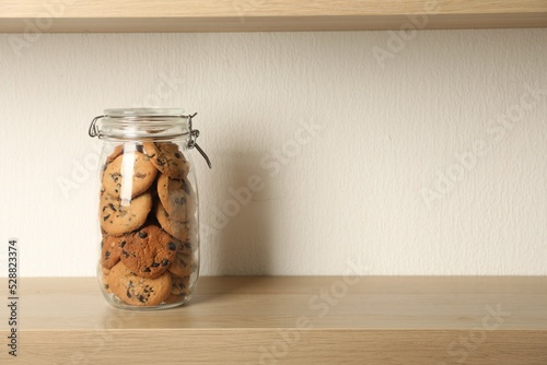 Delicious chocolate chip cookies in glass jar on wooden table, space for text photo