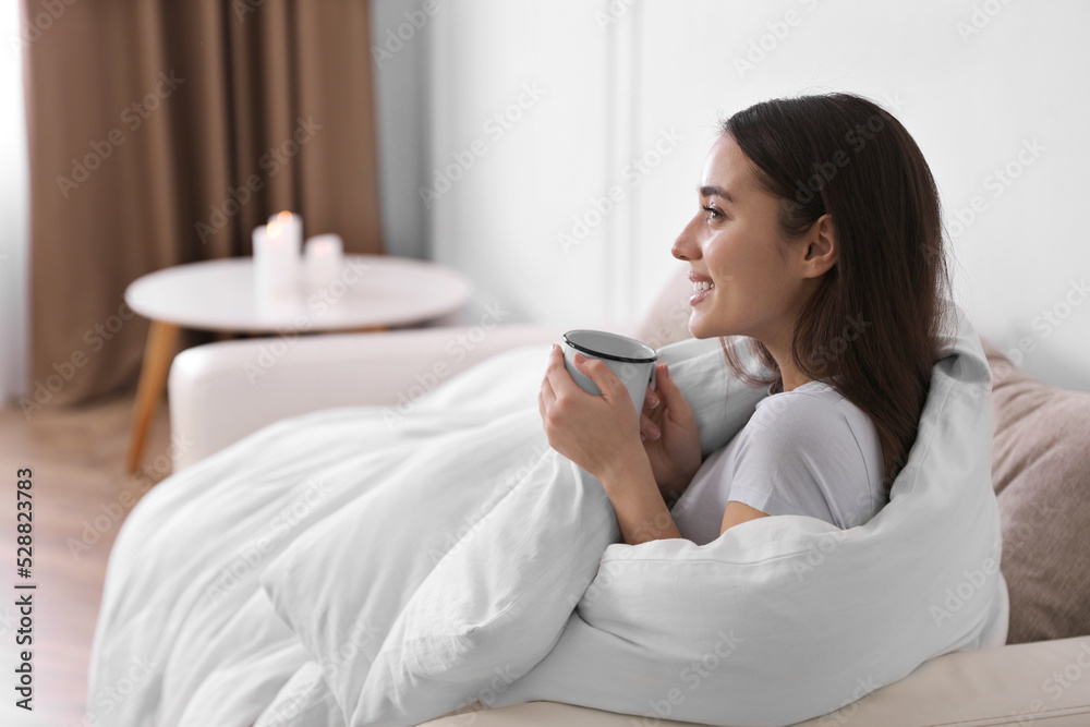 Woman covered in blanket holding cup of drink on sofa, space for text