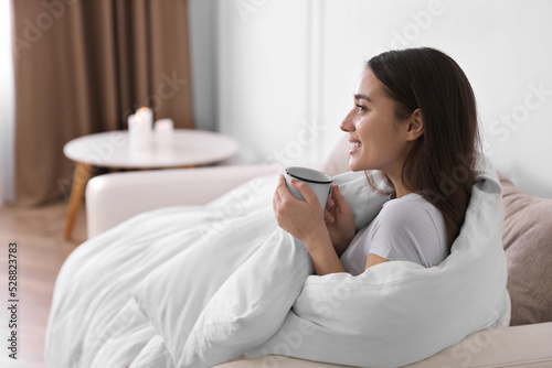 Woman covered in blanket holding cup of drink on sofa, space for text