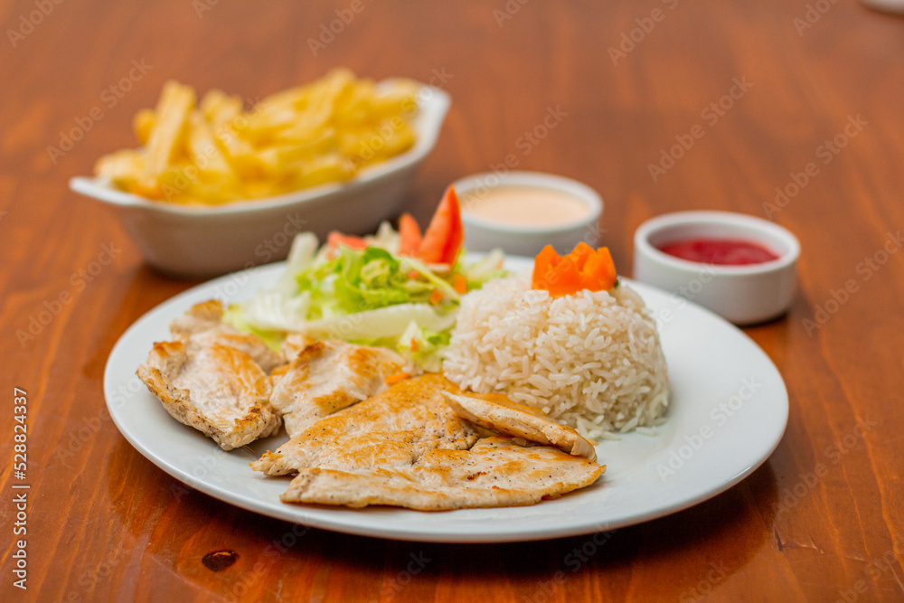 Grilled chicken accompanied by rice with french fries and salad.