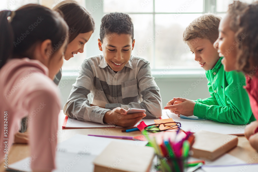 Excited Black Schoolboy Using Phone With Classmates In Modern Classroom Excited Black Schoolboy Using Phone With Classmates In Modern Classroom