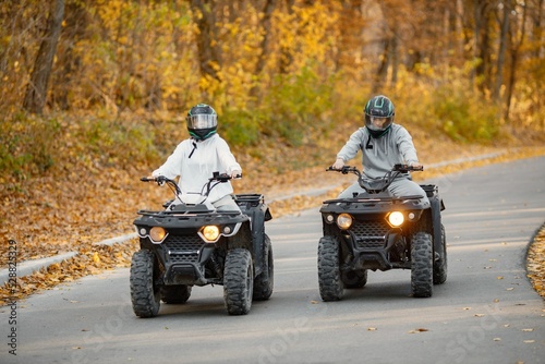 Man and woman driving quad bikes in autumn forest