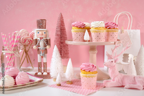 On trend pink Christmas children's party table with cupcakes, pink nutcracker, reindeer, mini trees, and decorations.