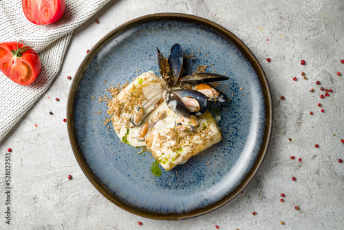 halibut steak on plate with mussels and creamy sauce on grey table top view