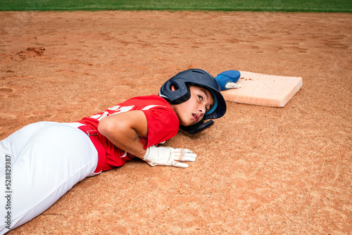 Teenage male baseball player sliding in the dirt to reach the base photo