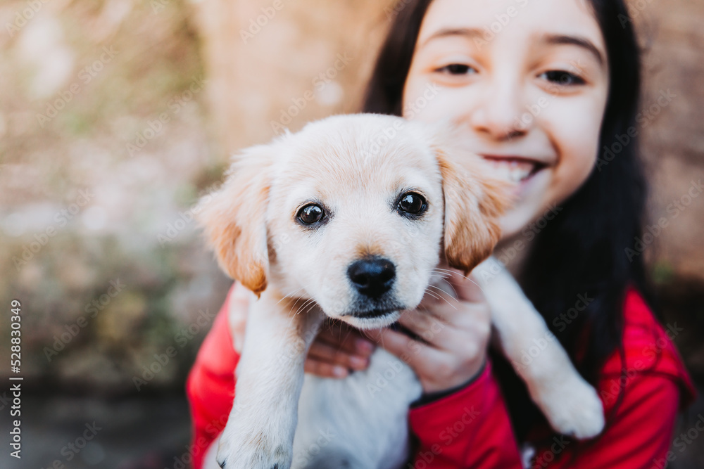 Smiling little girl embracing a golden retriever puppy in the park Smiling little girl embracing a golden retriever puppy in the park