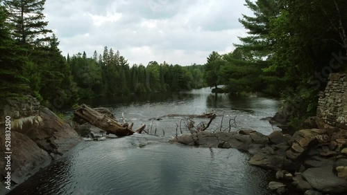 Aerial shot of the flowing Oxtongue River as the water passes through a rocky narrowing cascading over the edge of a waterfall pushing through trees and debris, Algonquin Provincial Park, Canada photo