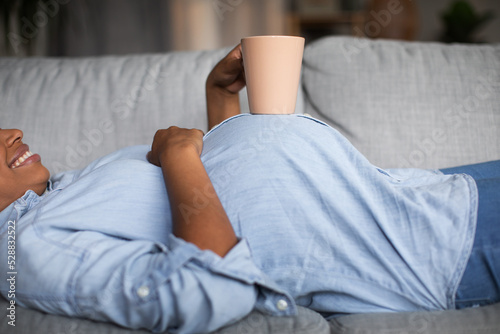 Unrecognizable Pregnant Black Female Holding Cup Lying On Sofa Indoor
